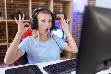 Young caucasian woman playing video games wearing headphones looking surprised and shocked doing ok...