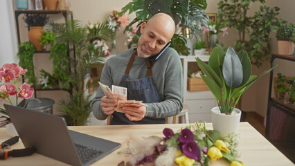 Hispanic bald man counts icelandic krona in a green plant-filled flower shop while talking on the...