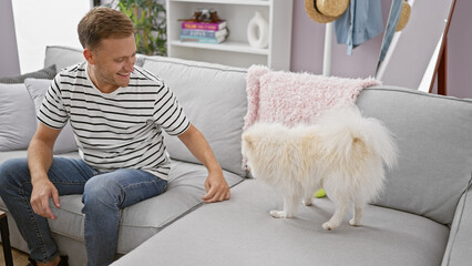 Confident young caucasian man happily enjoying a relaxing indoor play session with his beloved dog,...