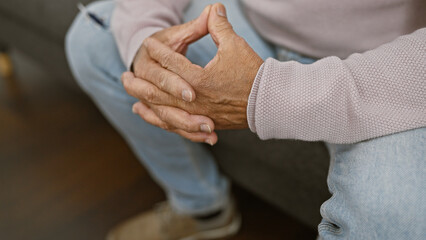 Close-up of a thoughtful senior man's hands clasped while seated indoors, suggesting contemplation.