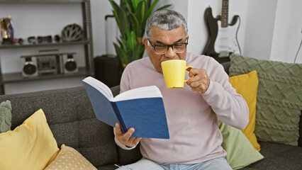 Mature man reading book and sipping coffee in a cozy living room.
