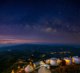 Tent Camping Village on mountain peak at night in starry sky with milky way at dawn