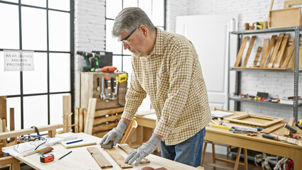 Mature man works diligently in a well-equipped carpentry workshop surrounded by tools and wood.