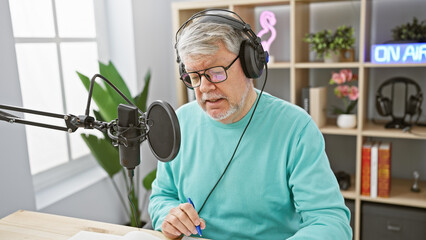 Mature man with headphones speaking into microphone in a bright radio studio.