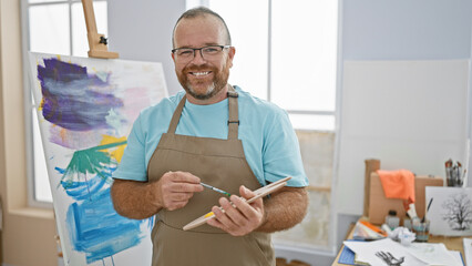 Smiling, confident caucasian man joyfully indulging in his art hobby, painting a canvas in a cozy...