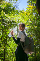 woman with backpack break to drinking water form bottle hiking and trekking in forest path