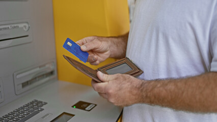 Attractive middle-aged caucasian man inserting credit card into street atm machine in urban city -...