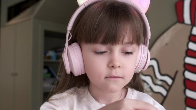 Close-up portrait of a little girl wearing headphones. Contemplative, dreamy facial expression. Looks into the distance. Child development concept.