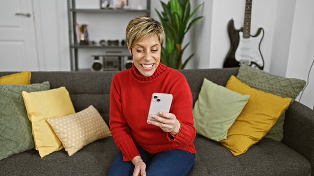 A smiling young hispanic woman with short blonde hair enjoying her time using a smartphone in a cozy living room.