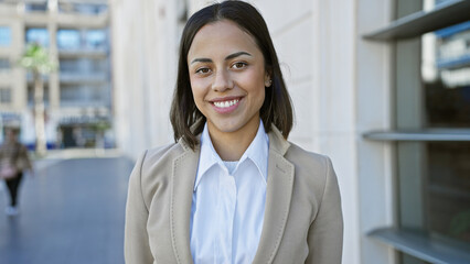 A smiling young hispanic woman stands confidently outdoors in a city environment, exemplifying...