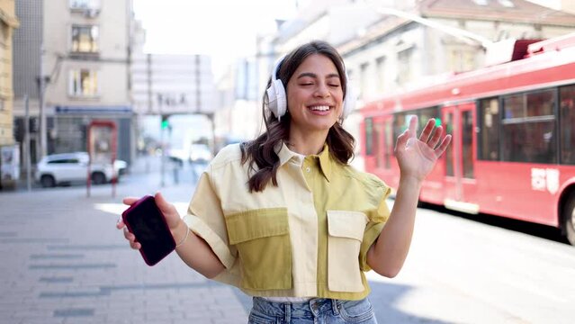 Happy young Mexican woman with headphones enjoying music on the street