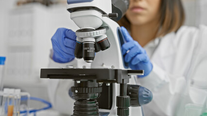Focused young scientist examining samples using a microscope in a laboratory environment,...