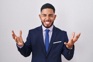 Young hispanic man wearing business suit and tie celebrating mad and crazy for success with arms...