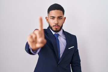 Young hispanic man wearing business suit and tie pointing with finger up and angry expression, showing no gesture