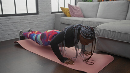 African american woman with braids exercising indoors on a yoga mat in a living room