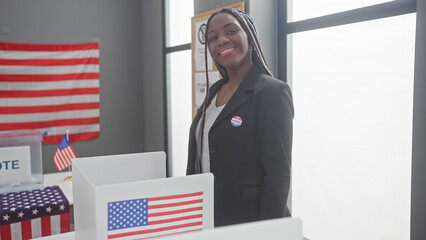 Portrait of a confident african american woman with braids wearing a 'voted' sticker indoors at a polling station with american flags.