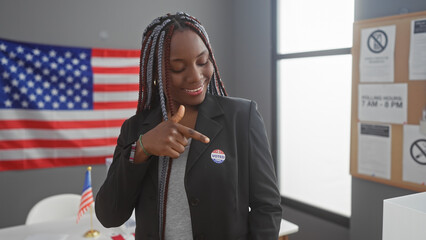Smiling african american woman with braids pointing to 'i voted' sticker in an electoral center...