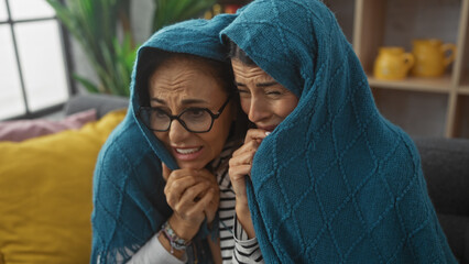 Two women sharing an emotional moment under a blue blanket on a couch at home