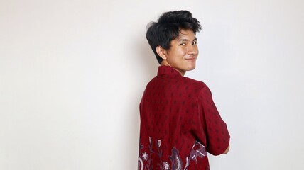 A handsome young Asian man wearing batik is posing facing forward and smiling