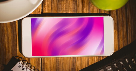 Image of smartphone with pink moving shapes on screen on wooden desk