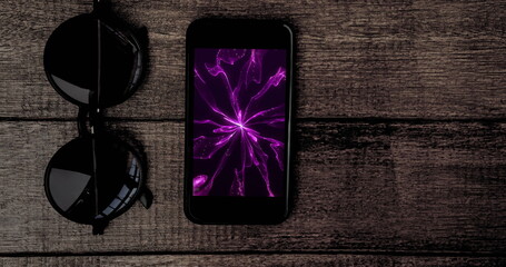 Image of smartphone with purple light trails on screen and sunglasses on desk
