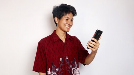 Handsome young Asian man wearing batik shows a happy smile on his smartphone