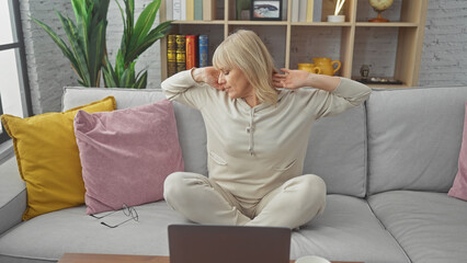 Blonde woman stretching on a sofa in a cozy living room, depicting relaxation at home.