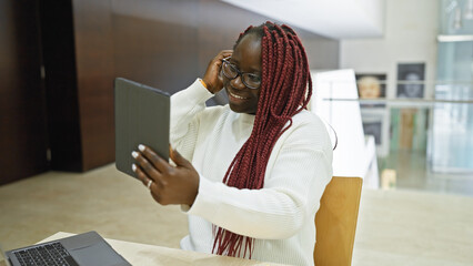 Smiling african american woman with braids using tablet in modern office interior