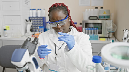 African female scientist with braids examining a sample in a laboratory setting, portraying professionalism and expertise.