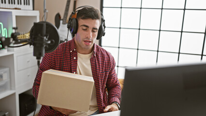 Young, handsome hispanic male musician showcasing a package during a video call in music studio...