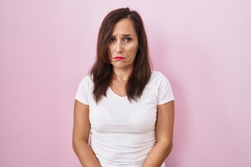 Middle age brunette woman standing over pink background depressed and worry for distress, crying...