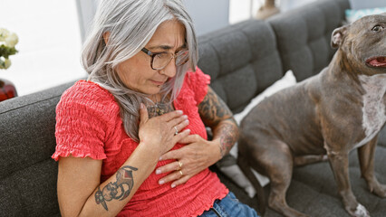 Heart-struck grey-haired middle age woman suffers attack in her cozy living room, sitting with...