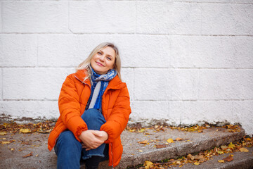 Happy smiling middle aged woman in orange down jacket sitting on concrete stairs outdoors © Dasha Petrenko