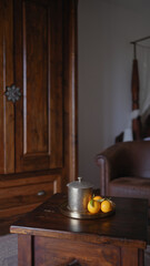 A vintage pewter teapot and fresh oranges on a wooden table set elegantly within a cozy, rustic interior.