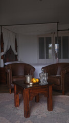 Elegant interior with vintage leather sofa, wooden table, silver teapot, glassware, and oranges.