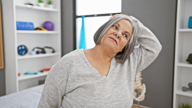 A senior woman stretches her neck in a physical therapy clinic, indicating healthcare, wellness, and rehabilitation.