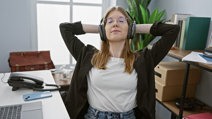 A relaxed young woman enjoying a break with headphones in a modern office setting.