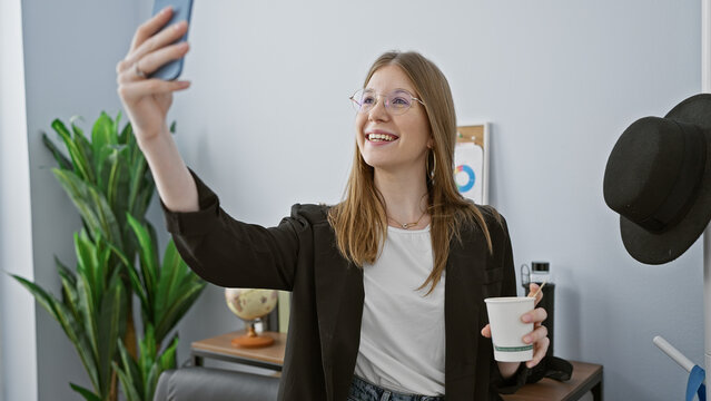 A smiling young woman takes a selfie at her modern indoor office, embodying a casual professional vibe.