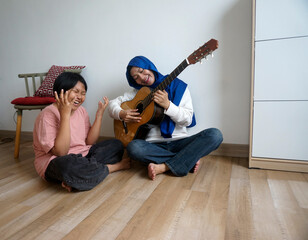 Asian muslim woman playing guitar and her daughter singing with deeply emotion at home. Concept of...
