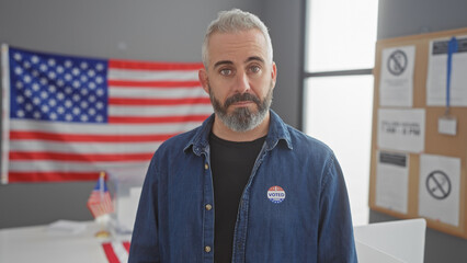 Portrait of a bearded man with a voting sticker standing in an american college's electoral center,...