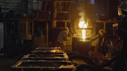 Industrial foundry workers pour molten metal with intense flames and smoke