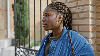 A contemplative african american woman with braids standing on an urban street against a brick...