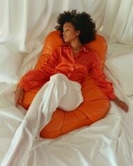 Young African-American Woman in Orange Pajamas Relaxing on a Bed - Serene Indoor Scene - obrazy, fototapety, plakaty
