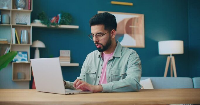 Man working with laptop. Male sitting at table and closing laptop. Man working at home office. Smiling man wearing glasses. Cozy flat. Male freelancing at home. Man satisfied with finishing work.