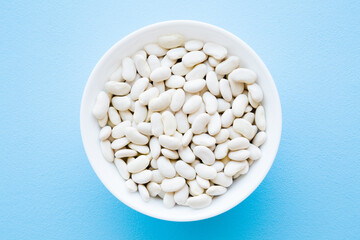 Fresh dry white beans in bowl on light blue table background. Pastel color. Healthy food. Closeup. Top down view.