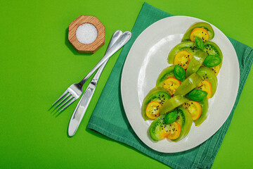 Fresh summer salad from green heirloom tomato Kiwi, fresh basil leaves and extra virgin olive oil