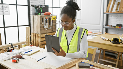 Focused african american woman using tablet in carpentry workshop