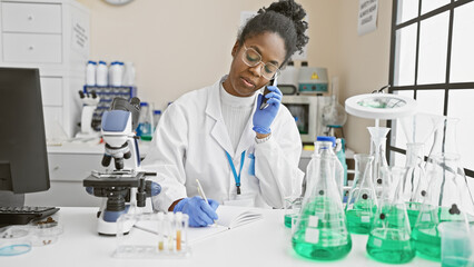 African american woman scientist analyzing samples while talking on the phone in a laboratory