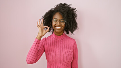 African american woman in glasses making the ok sign indoors with a pink background, exemplifying...