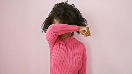 Black woman covering eyes with arm against pink background, depicting emotion or headache